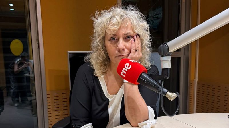 La periodista Sandra Urdín posa reflexiva en un estudio de RNE junto a un micrófono profesional con el logotipo de la emisora sobre un fondo de paneles acústicos.