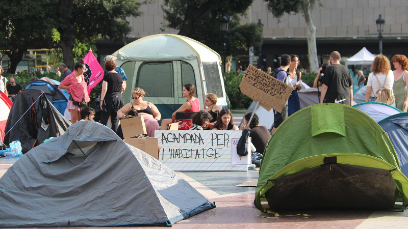 J�venes protestan en una plaza con tiendas de campa�a y carteles que dicen "ACAMPADA PER L'HABITATGE" y "WELCOME TO SPAIN TOURISTS, THIS IS THE REALITY OF THE COUNTRY".