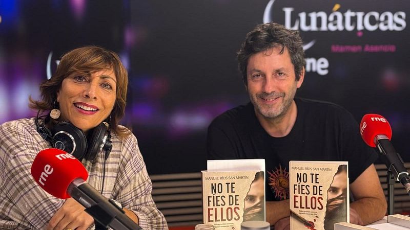 Mamen Asencio y Manuel Ríos San Martín sonríen en el estudio de RNE junto a micrófonos rojos y ejemplares del libro "No te fíes de ellos", bajo el cartel del programa "Lunáticas".