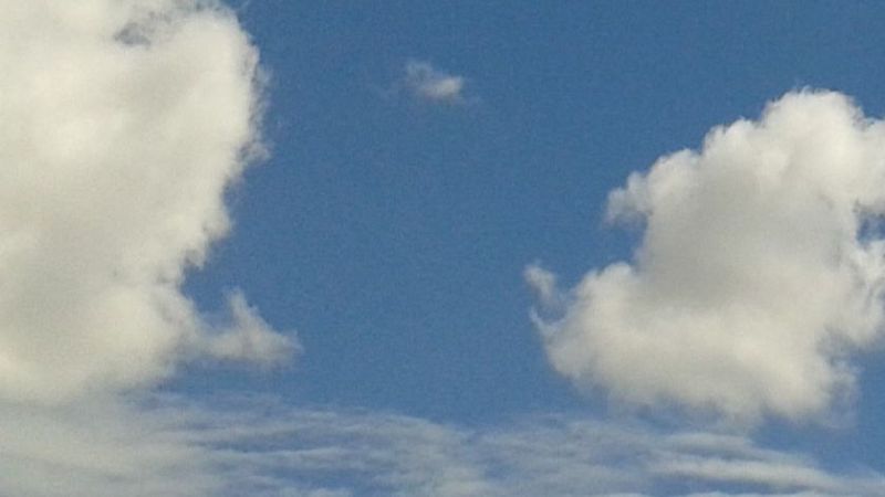 Vista de un cielo azul brillante enmarcado por nubes blancas y esponjosas en los laterales y una franja de nubes bajas y onduladas en la parte inferior durante el amanecer.