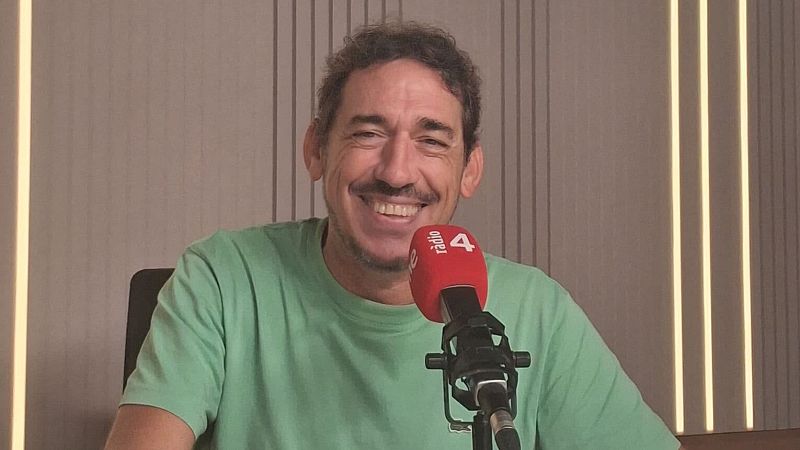 El presentador Oriol Clavell sonr�e en un estudio de radio frente a un micr�fono profesional con un antiviento rojo donde se lee "R�dio 4" y "rne".