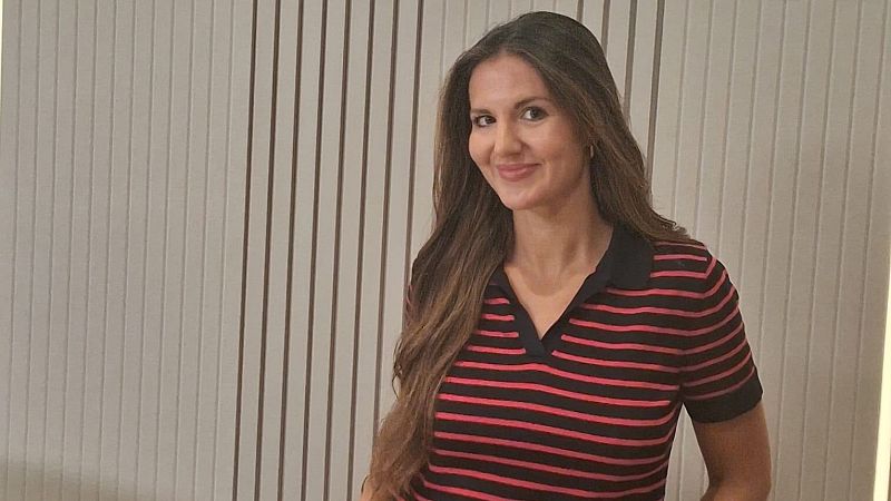 Retrato de la periodista Georgina Badenas sonriendo con un polo de rayas rojas y negras ante un fondo de listones de madera.