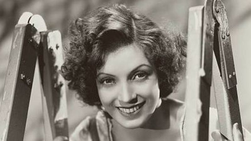 Retrato en blanco y negro de la actriz Conchita Montenegro sonriendo con el rostro enmarcado entre dos maderas de una escalera y luciendo un peinado con rizos de los años 30.
