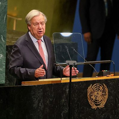 António Guterres, Secretario General de la ONU, gesticula durante un discurso en el podio oficial de la Asamblea General, vestido con traje oscuro y corbata rosa.