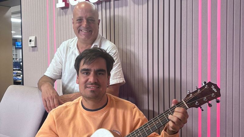 El cantautor Pau Alabajos posa con una guitarra Taylor junto a un compa�ero en el estudio de R�dio 4, decorado con luces de ne�n rosa.