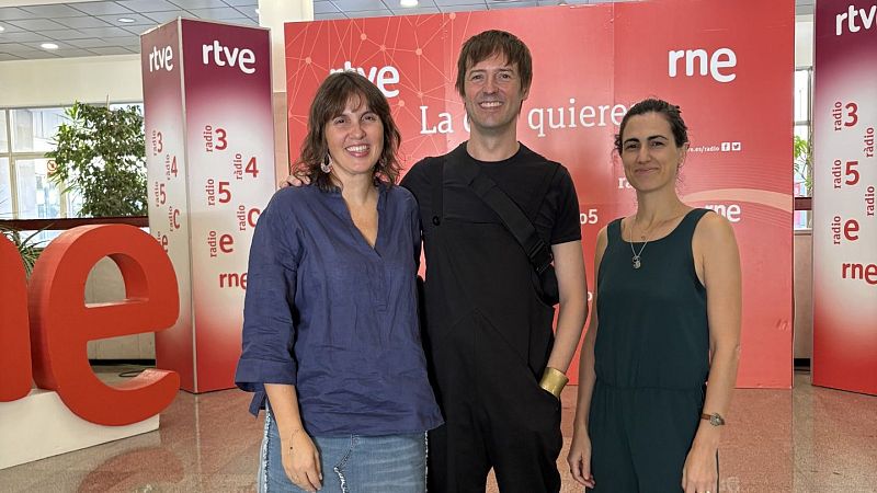 Sabela Mendoza, Javier Martín y Olga Baeza sonríen en el vestíbulo de RNE frente a un photocall corporativo rojo y blanco con logotipos de RTVE y grandes letras corpóreas.