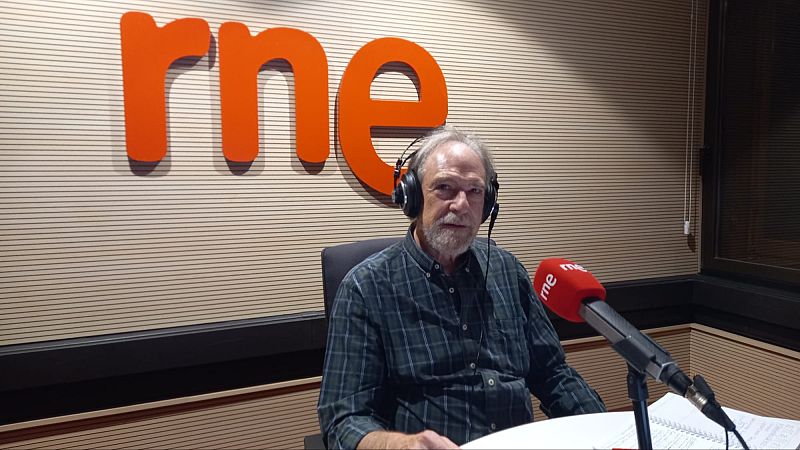 El periodista Josep Ramoneda, con auriculares y camisa de cuadros, mira a la cámara en un estudio de RNE frente a un micrófono con el logo de la emisora.