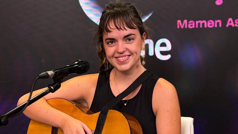 Joven música sonriente con guitarra y micrófono en estudio de radio, frente a un fondo corporativo con la luna y texto de RNE.
