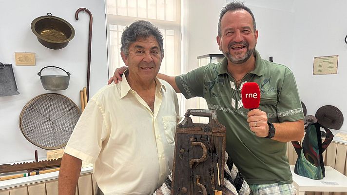 Dos hombres sonrientes posan en una sala del Museo de Instrumentos Folclóricos junto a una matraca tradicional y objetos etnográficos en las paredes.