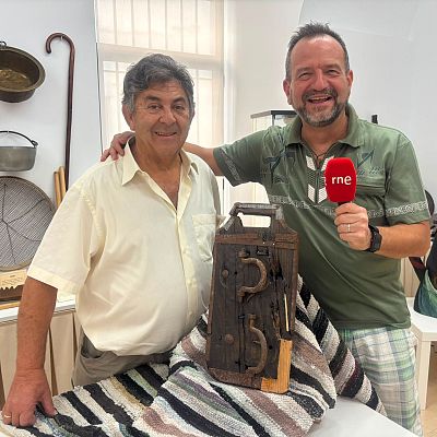 Dos hombres sonrientes posan en una sala del Museo de Instrumentos Folclóricos junto a una matraca tradicional y objetos etnográficos en las paredes.