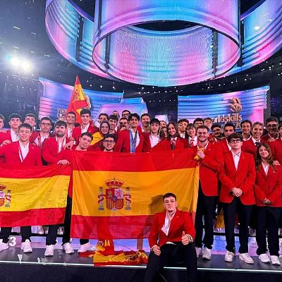 Delegación española posa con americana roja y banderas de España en el escenario iluminado de WorldSkills.
