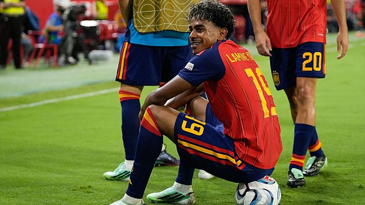 Lamine Yamal sonríe sentado sobre un balón de fútbol vistiendo la equipación de la Selección Española con el dorsal 19.