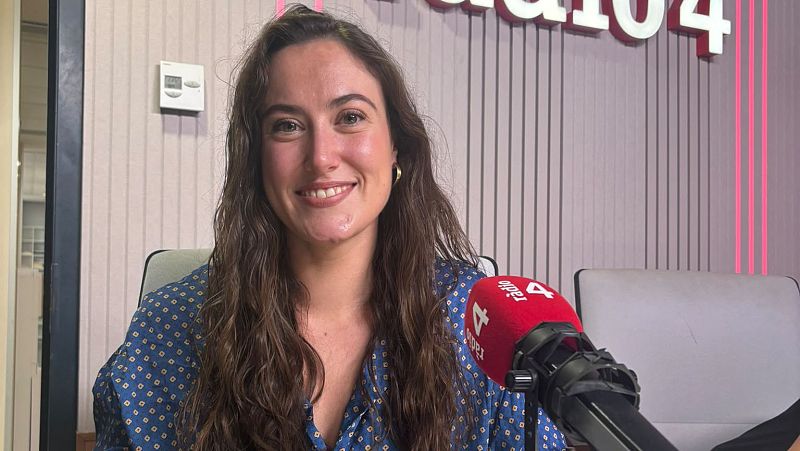 Una mujer joven sonr�e en un estudio de radio con paneles ac�sticos e iluminaci�n roja, junto a un micr�fono con capuch�n rojo.
