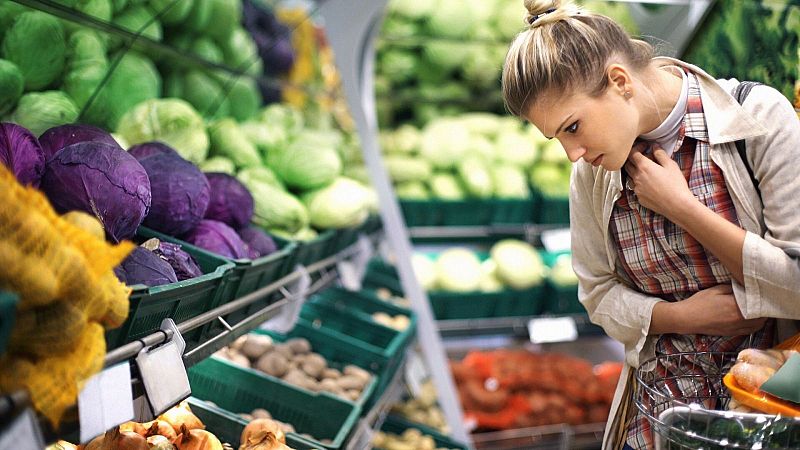 Una mujer joven con camisa a cuadros y cesta de la compra observa los productos frescos en la secci�n de fruter�a de un supermercado.