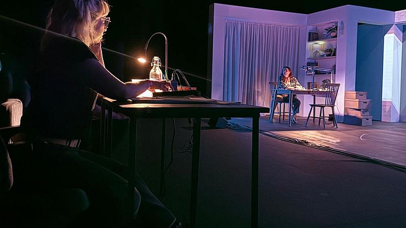 Ensayo teatral donde la directora Amaya Galeote observa desde la penumbra del patio de butacas a una actriz actuando en un escenario iluminado.