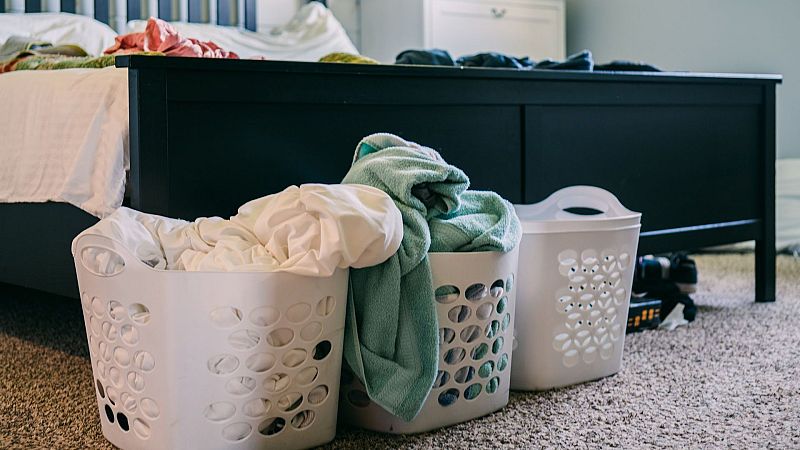 Tres cestos de pl�stico blanco con ropa y s�banas se encuentran sobre la moqueta al pie de una cama deshecha en un dormitorio.