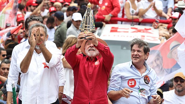 Luiz Inácio Lula da Silva sostiene una estatuilla religiosa junto a Elmano de Freitas y Cid Gomes durante un acto político multitudinario en un camión de campaña.