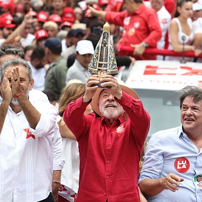 Luiz Inácio Lula da Silva sostiene una estatuilla religiosa junto a Elmano de Freitas y Cid Gomes durante un acto político multitudinario en un camión de campaña.