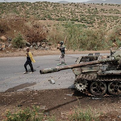Tanque militar destruido y oxidado, con impactos de proyectiles, abandonado junto a una carretera montañosa.