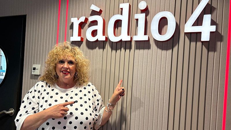 La periodista Silvia Tarragona sonr�e en un estudio de radio, se�alando un logotipo corporativo con luces rojas.