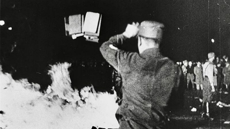 Fotograf�a hist�rica en blanco y negro de la quema de libros nazi en 1933, mostrando a un joven uniformado lanzando libros a una gran hoguera.