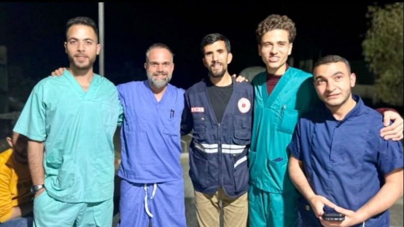 Cinco sanitarios posan sonrientes y abrazados de noche en el exterior, destacando Ra�l Incertis en el centro con pijama quir�rgico azul junto a compa�eros con uniformes m�dicos.