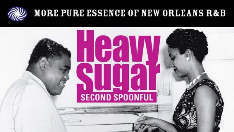 Portada musical con la imagen en blanco y negro del cantante Fats Domino y una mujer, sobre un fondo con los textos 'MORE PURE ESSENCE OF NEW ORLEANS R&B' y el título fucsia 'Heavy Sugar'.