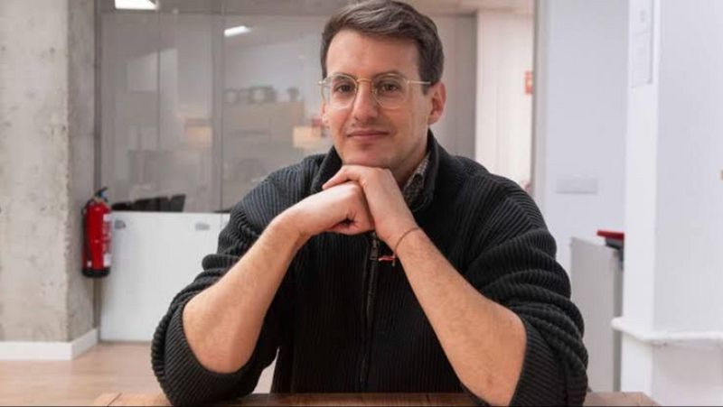Plano medio de Jorge Pueyo sentado ante una mesa, apoyando el mentón en sus manos entrelazadas con expresión serena.