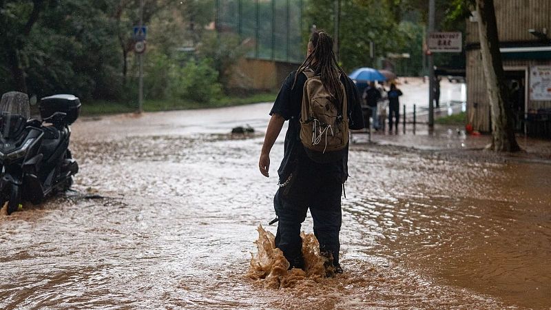 Una persona camina de espaldas por una calle completamente inundada de agua fangosa, levantando salpicaduras a su paso.