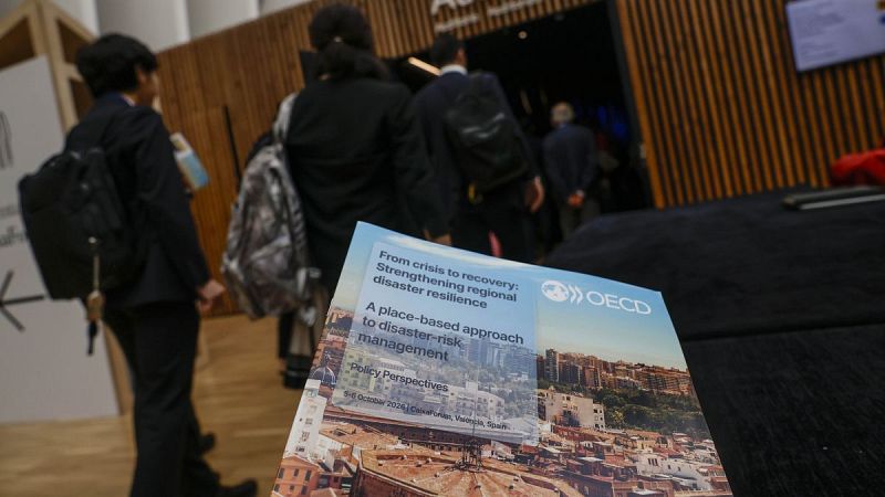 Portada de un informe de la OCDE sobre resiliencia regional ante desastres y asistentes caminando hacia una sala de conferencias.