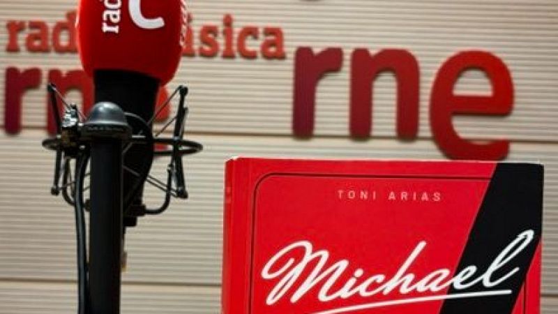 Micr�fono de estudio con capuch�n rojo y libro de canto titulado �Michael� de Toni Arias sobre una mesa en un estudio de radio.