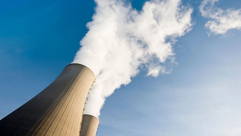 Dos torres de refrigeración grises, con forma cónica, liberan vapor blanco hacia un cielo azul claro. La imagen, tomada desde abajo, destaca la magnitud de las estructuras.