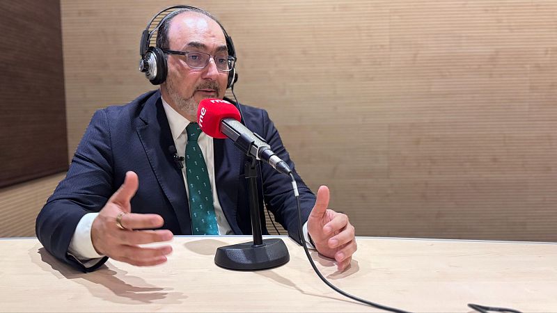 Plano medio de Sergio Díaz-Granados con traje formal, auriculares y micrófono de RNE en un estudio de radio.