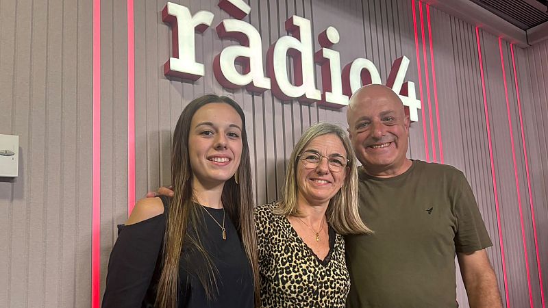 Tres personas posan sonrientes y abrazadas en un estudio de radio con luces LED magenta y el logotipo corporativo al fondo.