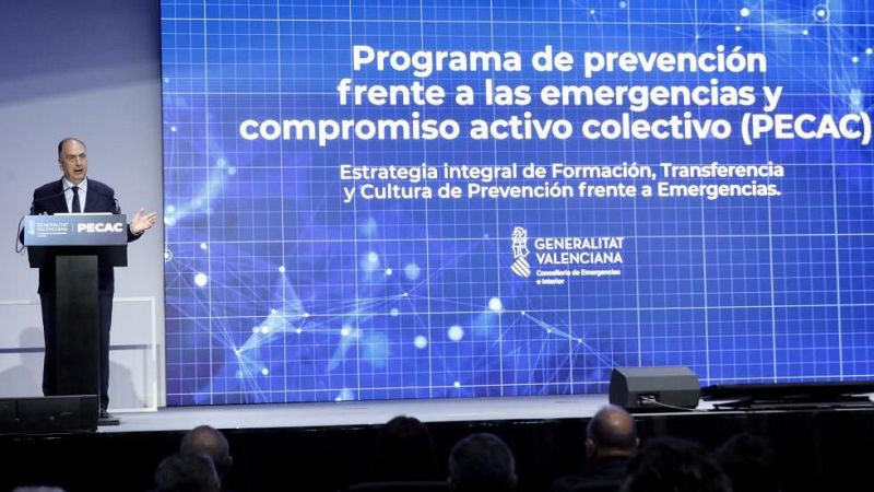 Orador interviniendo en un auditorio ante una pantalla con el programa PECAC de la Generalitat Valenciana.