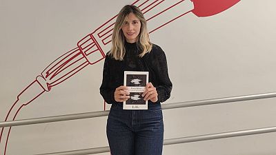 La escritora Paula Klein posa en un estudio de radio sosteniendo su novela �El amor inventado� frente a una pared decorada con un micr�fono vintage.