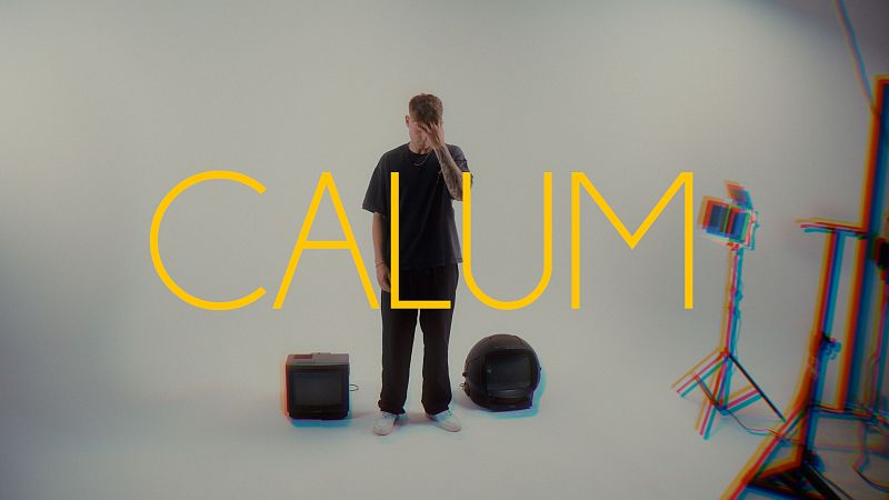 El cantante Calum posa pensativo en un plat� con fondo blanco junto a televisores antiguos y focos de estudio.