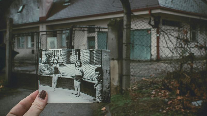 Mano sosteniendo una foto en blanco y negro de tres ni�as que contrasta con el paisaje actual deteriorado y oto�al.
