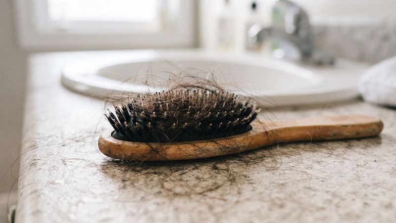 Primer plano de un cepillo de madera sobre una encimera, con las cerdas llenas de cabellos casta�os enredados.
