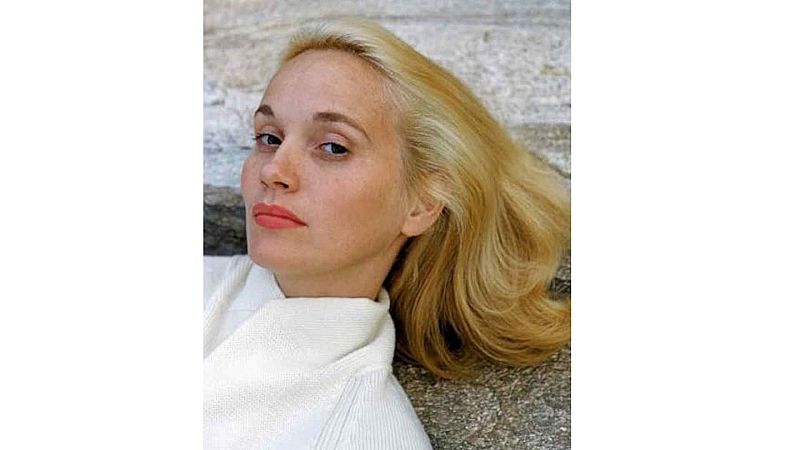 Retrato en plano medio de la actriz Eva Marie Saint con melena rubia, mirada directa y prenda blanca, apoyada sobre piedra.