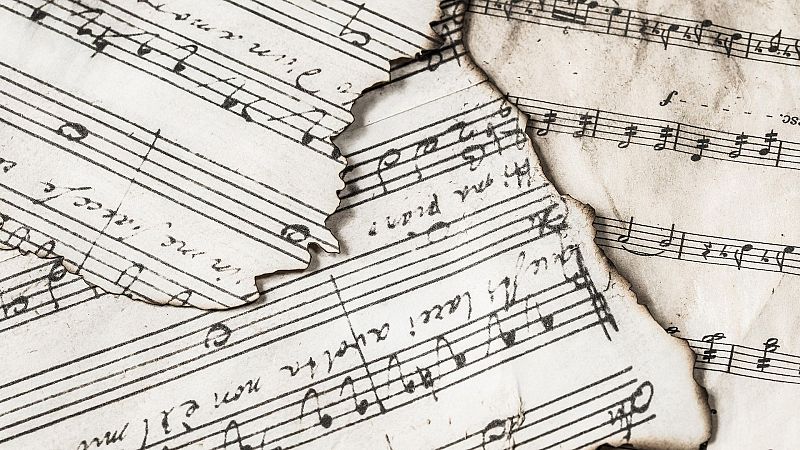 Plano de detalle de hojas de partituras musicales antiguas con bordes carbonizados y notas escritas a mano sobre papel envejecido.