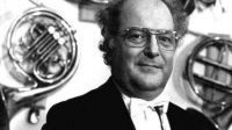 Retrato en blanco y negro del m�sico Gerd Seifert con traje formal y gafas, posando ante una pared con instrumentos de viento.