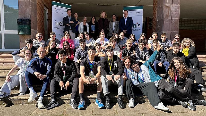 Fotografía de un grupo de jóvenes y adultos posando al aire libre frente a un edificio con paneles del Proyecto Horis.