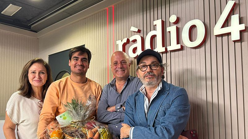 Cuatro personas posan sonrientes en un estudio de radio con paneles de madera y el logotipo de r�dio 4, destacando una cesta de frutas.