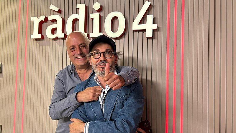 Dos hombres sonrientes posan en una emisora de radio, donde uno de ellos abraza afectuosamente al periodista Santi Villas, que lleva gorra y chaqueta vaquera.