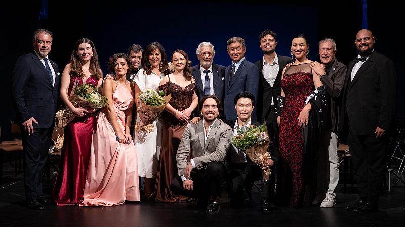 Pl�cido Domingo posa junto a un grupo de j�venes cantantes l�ricos y colaboradores en un escenario teatral tras una gala de zarzuela.