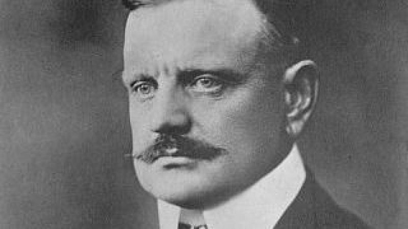 Retrato en blanco y negro de Jean Sibelius con expresi�n seria, cabello corto, bigote y vestimenta formal de principios del siglo XX.