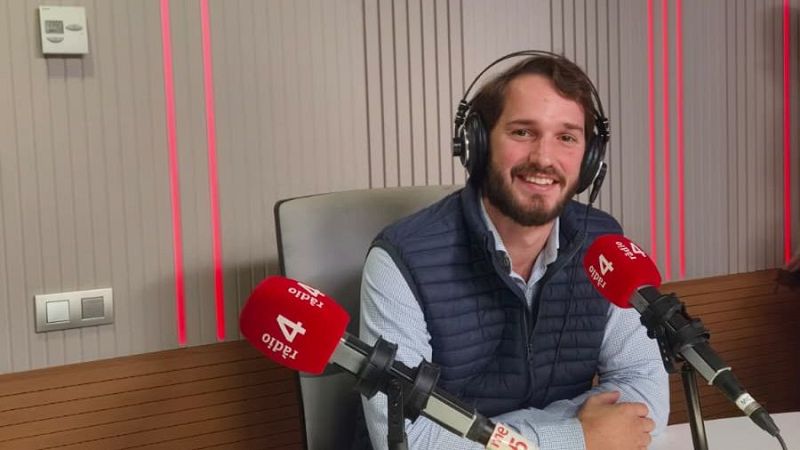 Joven locutor sonriente en un estudio de radio, con auriculares y micr�fonos con la marca r�dio 4, ante paneles ac�sticos iluminados.