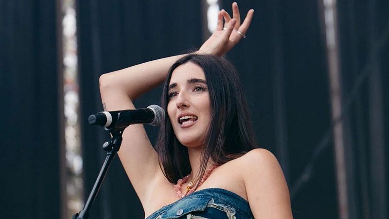 Judeline canta en directo sobre el escenario con un top vaquero y un brazo levantado.