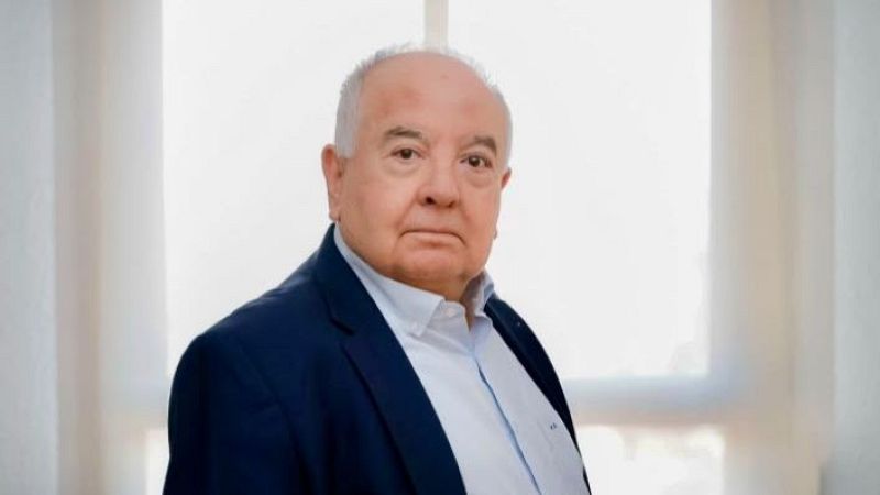 Retrato de medio corto de Antoni Bolinches con expresi�n seria, vistiendo chaqueta azul y camisa blanca ante un fondo iluminado por una ventana.